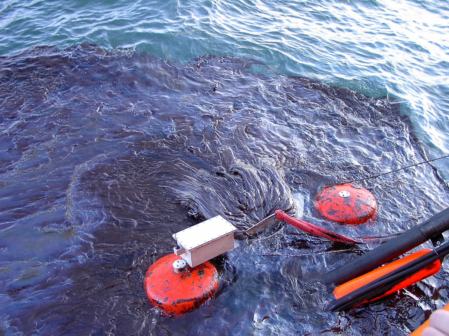 Oil spill in the ocean with containment equipment and floating barriers.
