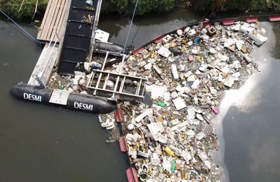 DESMI waste collection system intercepting floating debris in a river.