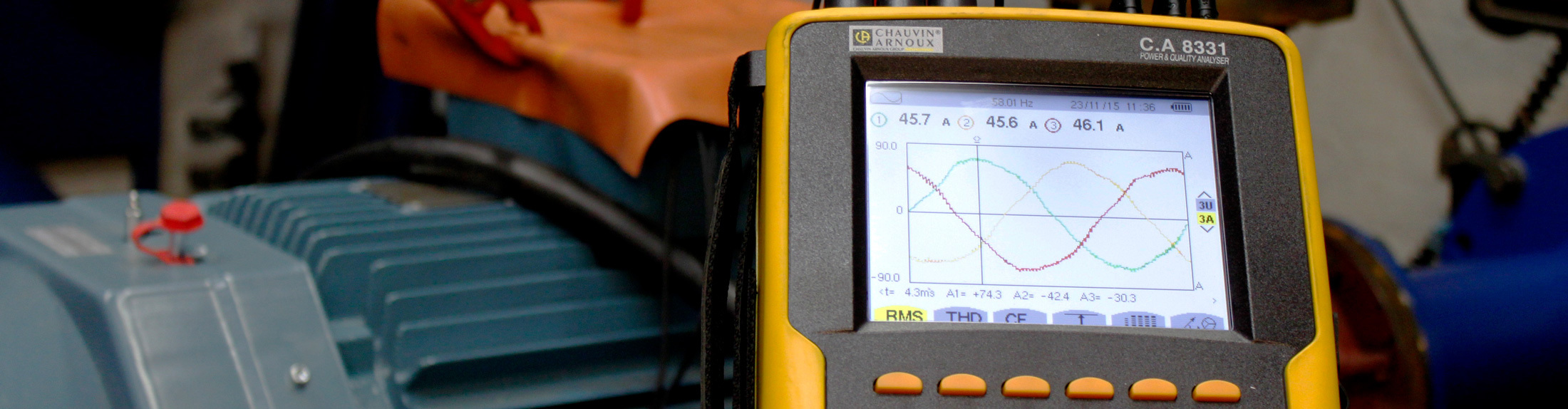 Yellow power quality analyzer displaying waveforms near industrial equipment.
