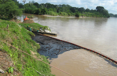 Oil spill containment boom in river with workers on the bank.