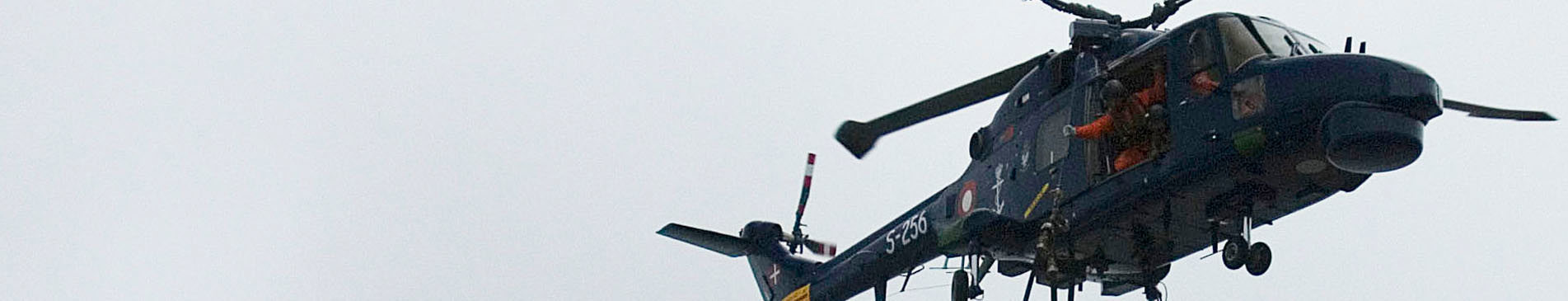 A helicopter in flight against a gray sky, with visible crew inside.