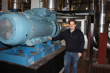 Man standing beside large industrial pump in a mechanical room.