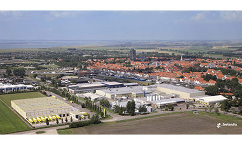 Aerial view of industrial complex and town with fields and distant coastline.